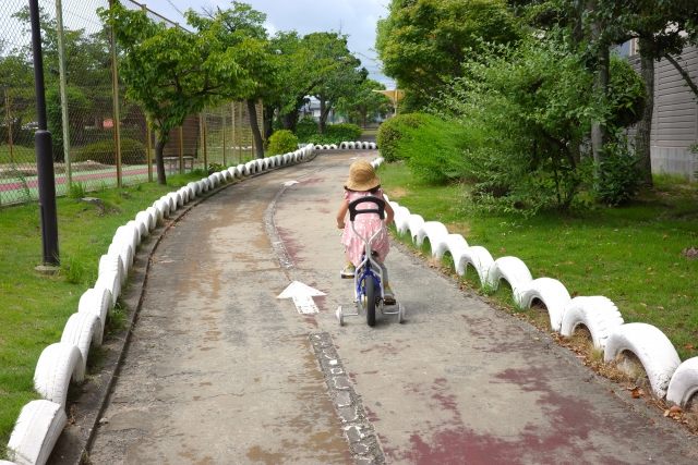 公園の遊歩道で5歳の子供が補助輪付き自転車の練習をしている様子
